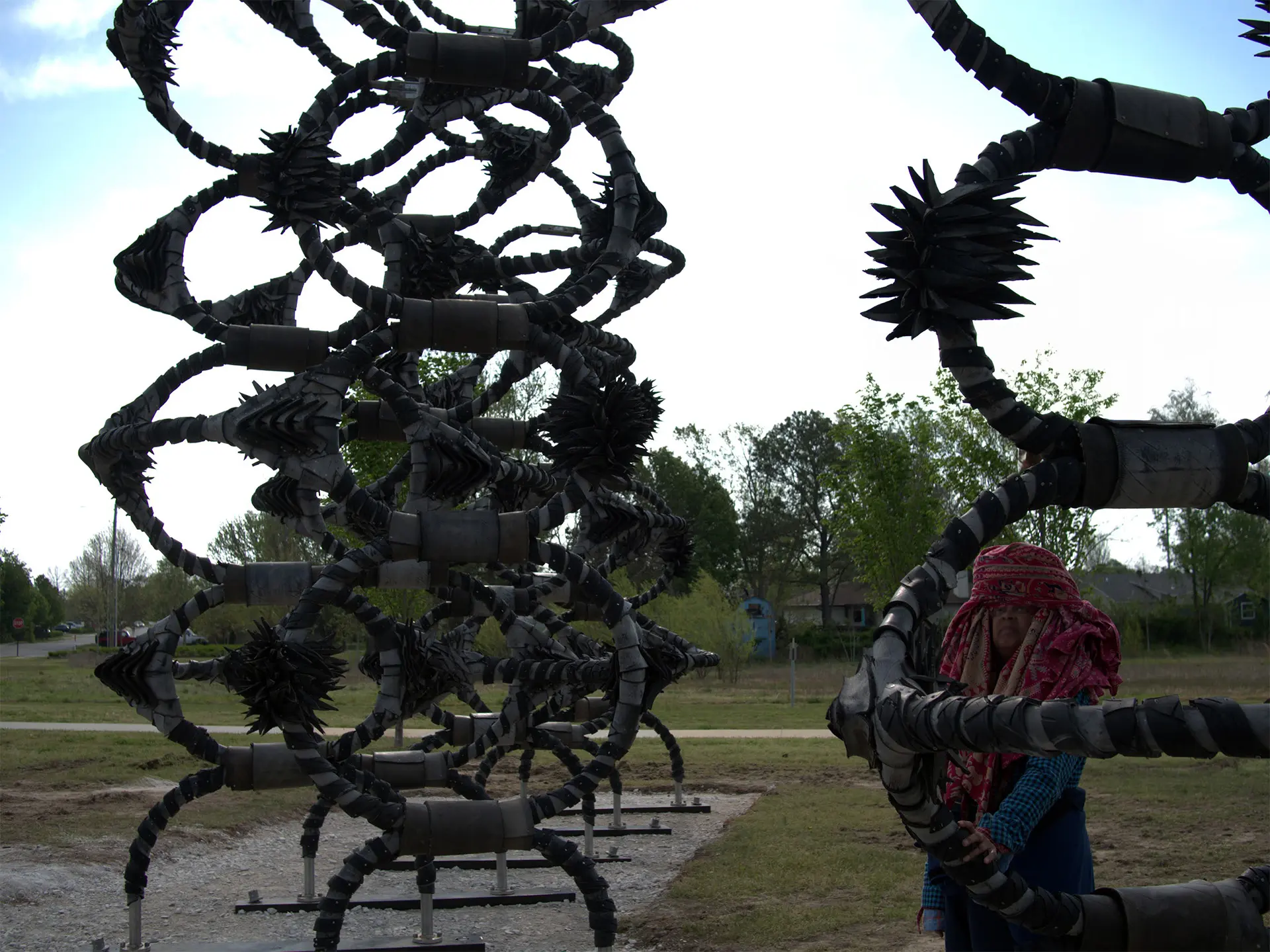 Shaved Portions by Chakaia Booker, towering black looping tire-and-steel forms in Osage Park, with a person standing beside it