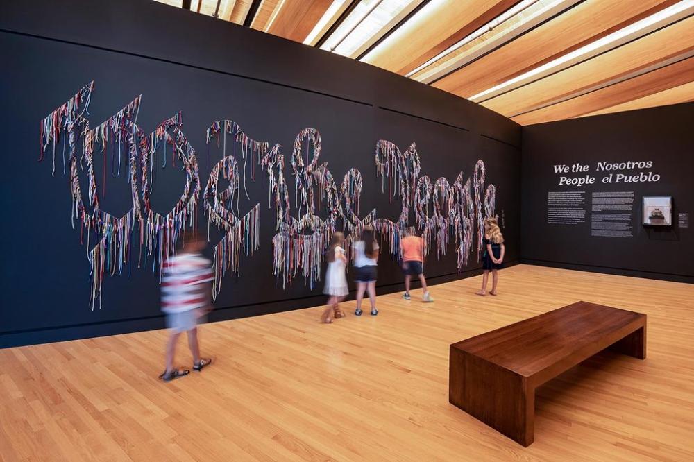 We the People by Nari Ward, the words spelled in colorful shoelaces across a dark gallery wall at Crystal Bridges